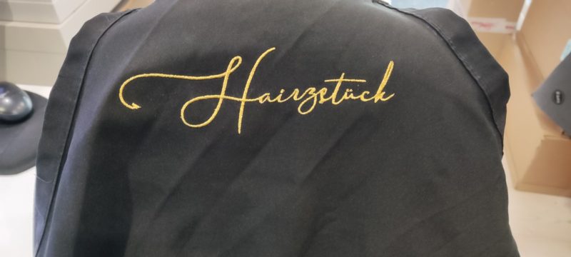 Dunkle Schürze mit goldfarbenem gesticktem Schriftzug