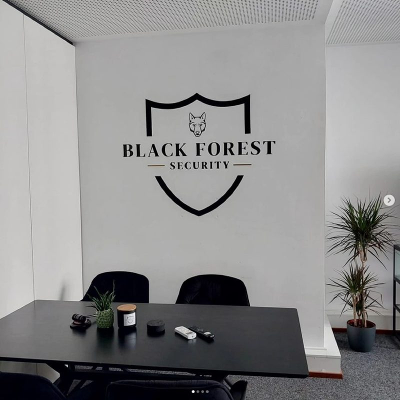 Weiße Wand mit großem schwarzem Firmenlogo über einem Besprechungstisch